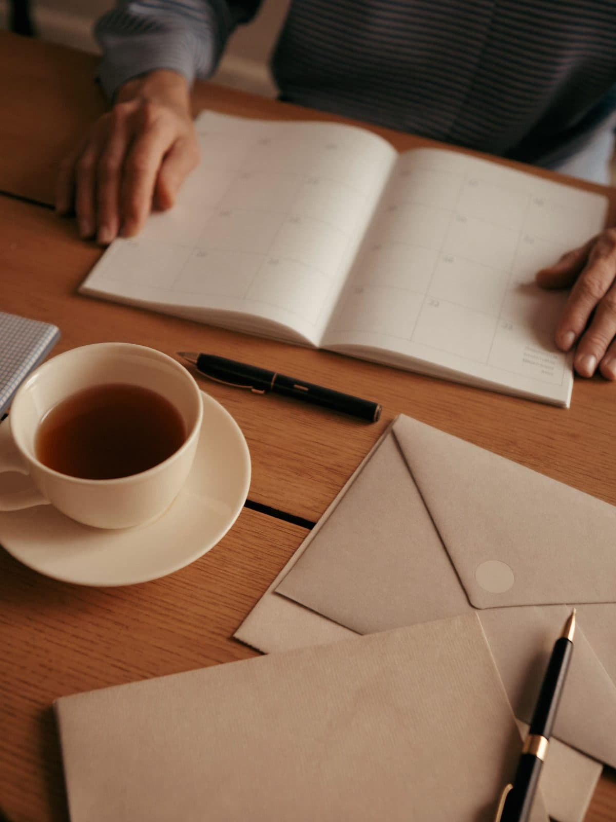 Ein aufgeschlagener Kalender, eine Tasse Tee und Briefumschläge auf einem Holztisch.